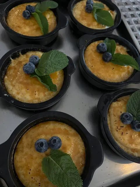 Crème brûlée in kleinen schwarzen Förmchen mit Heidelbeeren und Minze