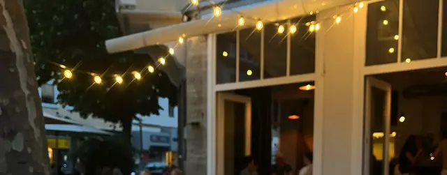 Terrasse des Café Heidelberg am Abend: Lichterkette unter der Markise, Gäste vor den hell erleuchteten Fenstern